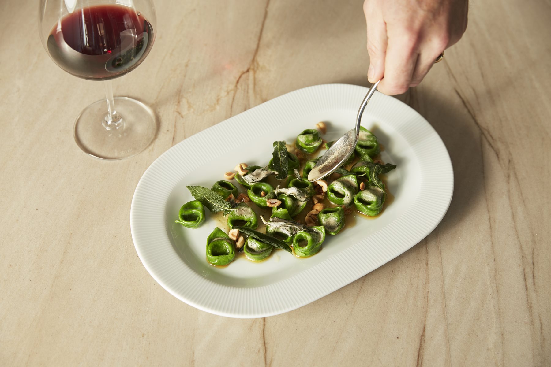 amare green pasta dish with glass of red wine
